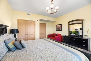 A bedroom with a large bed, a dresser, a red sofa, a television, and a chandelier. - Vacation Destination: Where Your Getaway Begins (Pigeon Forge)