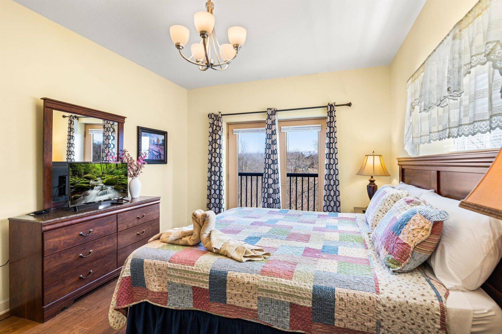 A bedroom with a large bed, a dresser, a television, and a window with curtains.