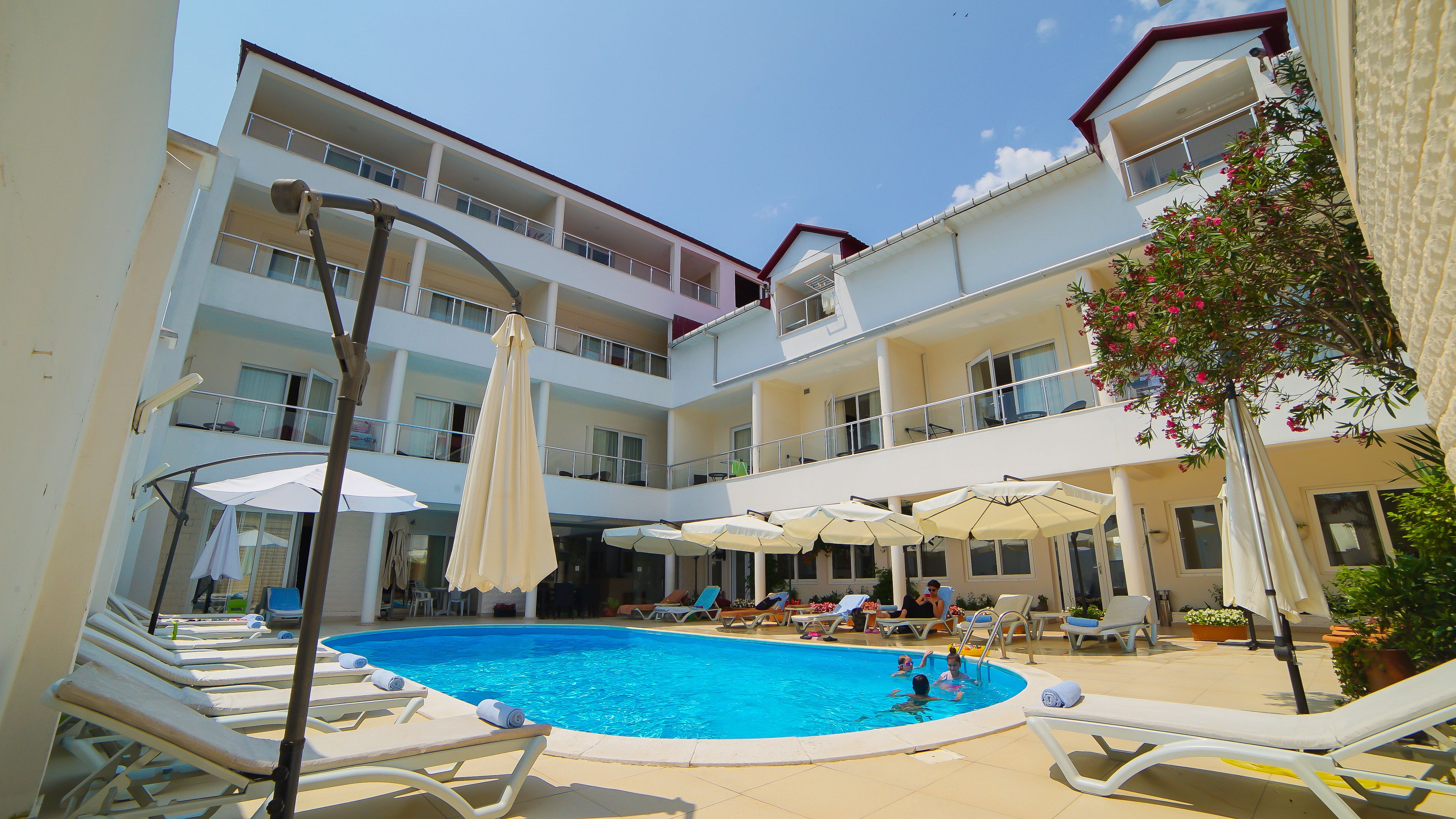 Et hotel med flere etager, swimmingpool, liggestole og parasoller.
