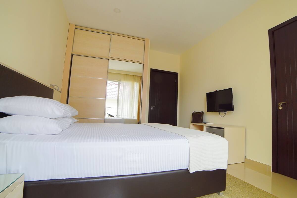 A bedroom with a large bed, a TV mounted on the wall, and a wardrobe.