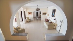 Un ampio soggiorno con soffitto alto, un lampadario e vista attraverso un arco.