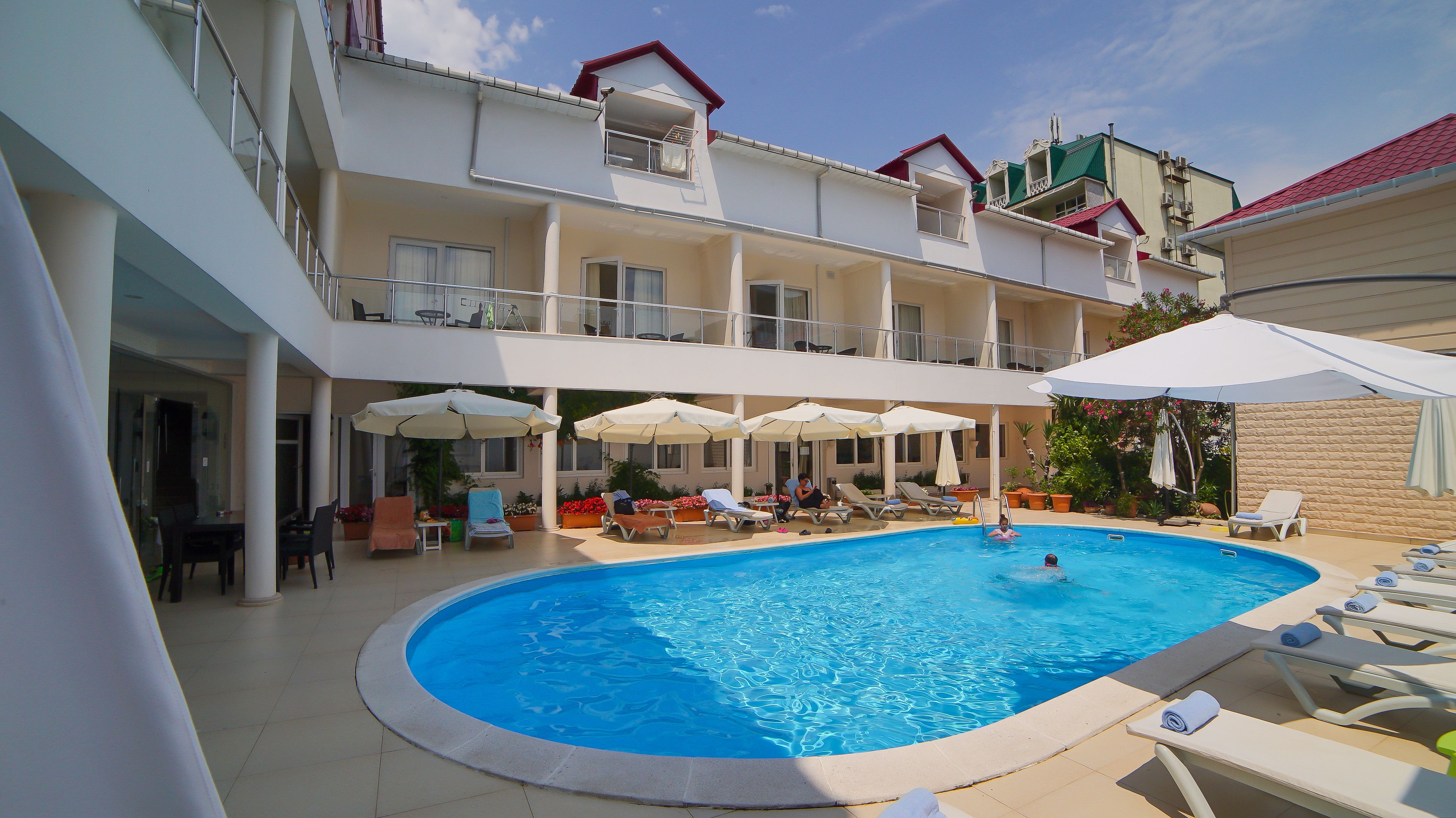 Una piscina con sillas de descanso y sombrillas, rodeada por un edificio de varios pisos con balcones.