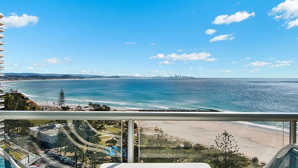 A balcony with a view of the beach and ocean, a parking area, and a building with a blue roof. - Ocean Plaza 1466 - Coolangatta Beachfront - Min. 3 Night Stays! (Coolangatta)