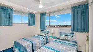 A bedroom with two beds, a ceiling fan, and a view of the city. - Ocean Plaza 1466 - Coolangatta Beachfront - Min. 3 Night Stays! (Coolangatta)