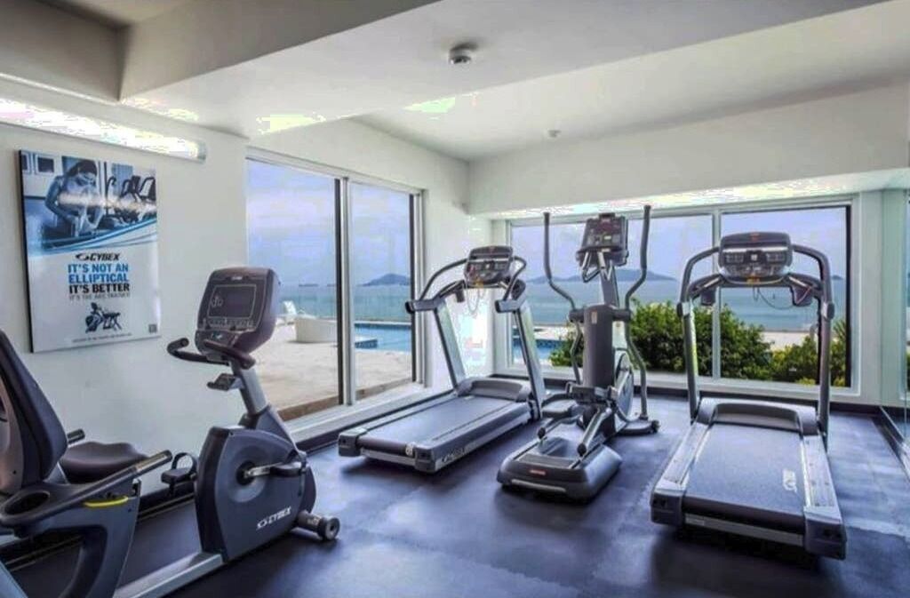 Une salle de sport équipée de tapis de course, d’un vélo elliptique et d’un vélo d’appartement, avec une grande fenêtre donnant sur la mer.