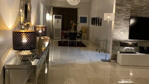 A modern living room with a large TV, a dining area with a chandelier, and a stone accent wall. - Luxuriously furnished modern home with open-plan design. Tema Spintex (Tema)