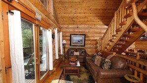 Ein Holzblockbau-Innenraum mit Ledersofa, Holztisch und einer Treppe.