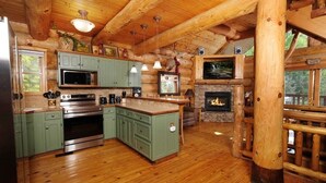 Ein Holzblockhaus-Innenraum mit einer Küche, die grüne Schränke, einen Kamin aus Stein und Holzböden zeigt.