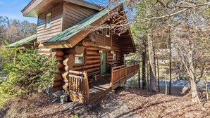 Eine Blockhütte mit grüner Tür, einer Veranda und einer kleinen Terrasse.