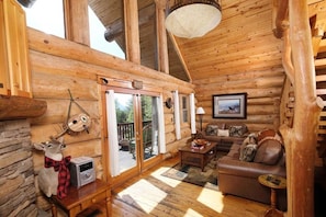 A log cabin interior with a wooden floor, a sofa, a table, and a deer head decoration.