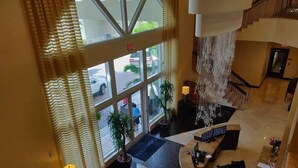 A hotel lobby with a reception desk, seating area, and large windows overlooking the street. - One bedroom apt just 1 mile to the beach with pool, gym, and playroom! (Boynton Beach)