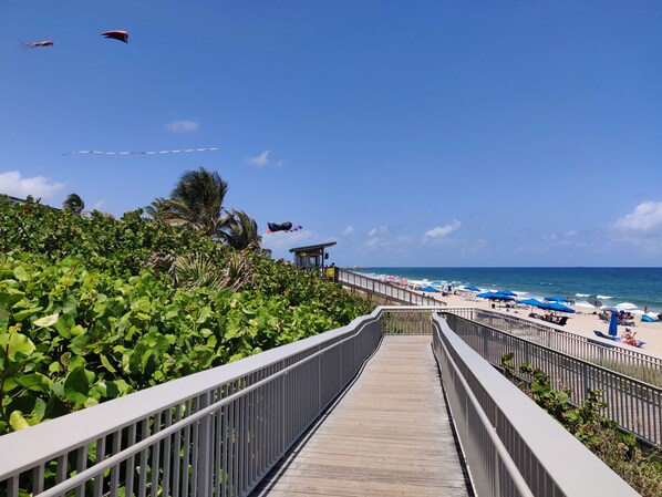A wooden boardwalk leading to a beach with umbrellas and lounge chairs.