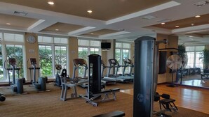 A spacious gym with various cardio and strength training equipment, large windows, and a mirror reflecting the space. - One bedroom apt just 1 mile to the beach with pool, gym, and playroom! (Boynton Beach)