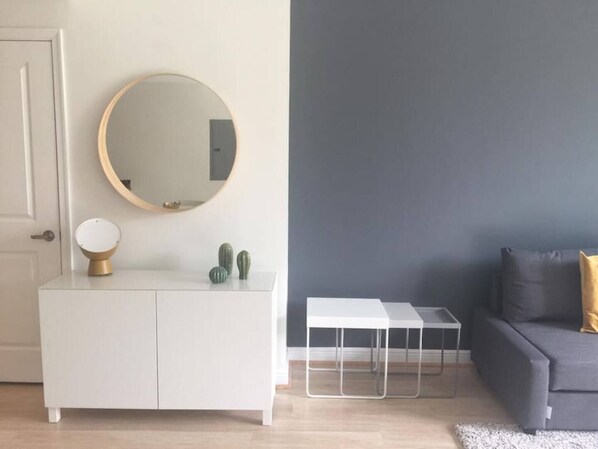 A modern living room with a white cabinet, a round mirror, a small table, and a gray sofa.