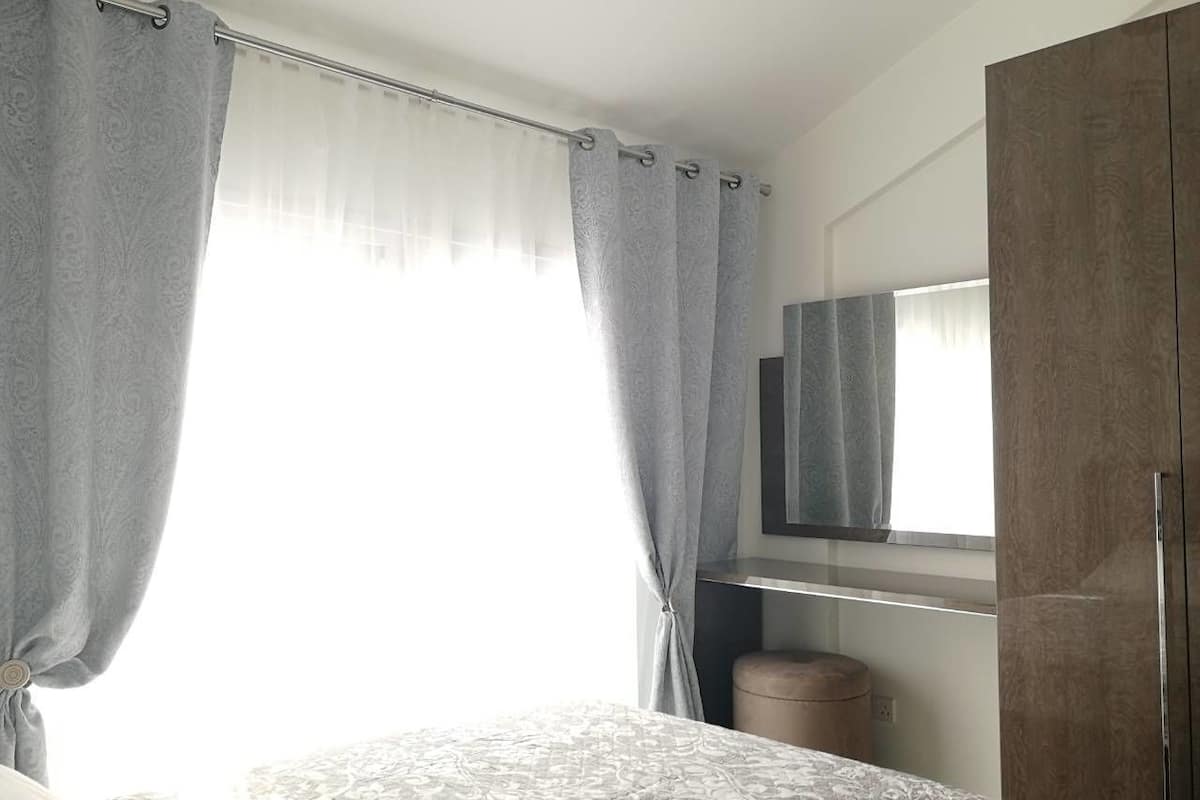 A bedroom with a bed, a wardrobe, a mirror, and a window with curtains.