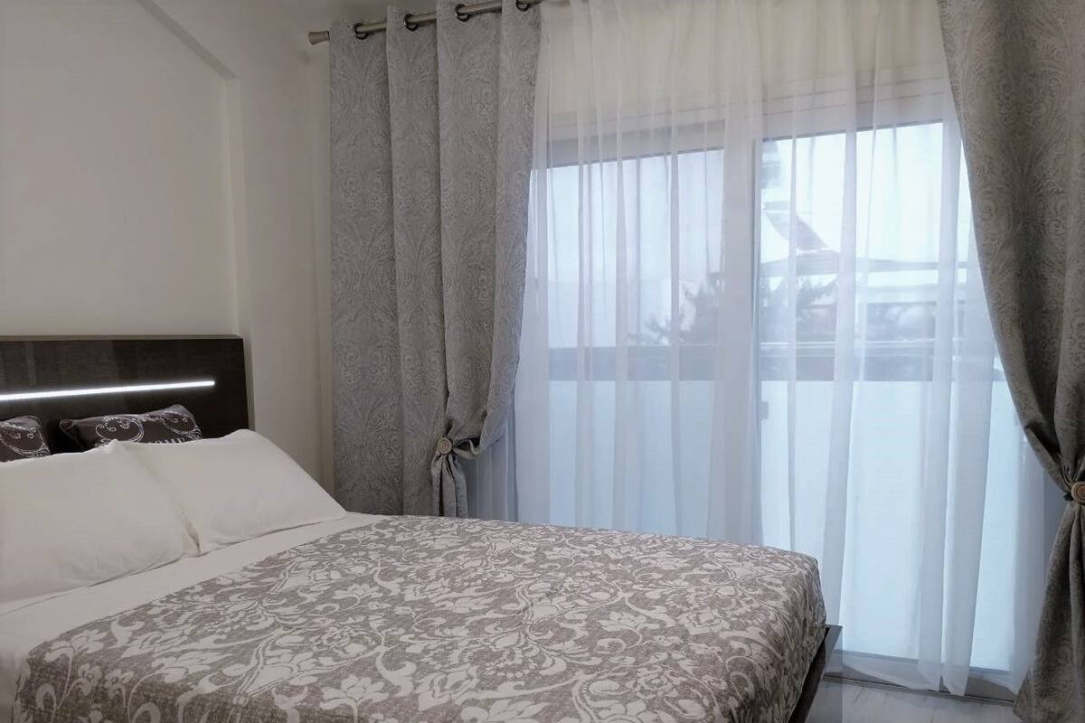 A bedroom with a large bed, a headboard, and sheer curtains.