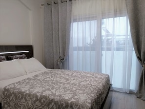 Un dormitorio con una cama grande, cabecera y cortinas traslúcidas.