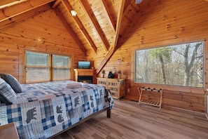 Camera da letto in una baita di legno, con un letto, una televisione, un camino e una finestra vista alberi.