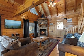 Interno di una baita di legno con camino in pietra, mobili in legno e vista sulla natura.