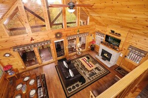 A spacious cabin with a high ceiling, wooden walls, a fireplace, a television, and a dining area with a table and chairs.