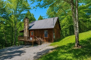 En rustik hytte med skorsten i sten, træfacade og en veranda med en rødlakeret dør.
