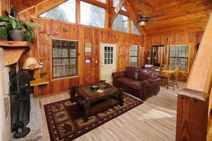 A wooden cabin interior with a wooden floor, a brown leather sofa, a wooden coffee table, and a ceiling fan. - River Romp: Splash Into the Smokies (Pigeon Forge)