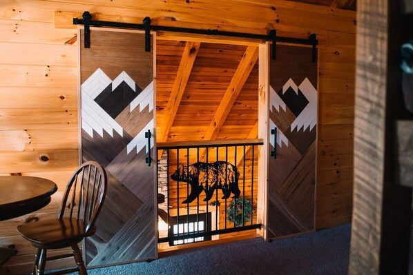 A wooden cabin interior with a dining area, a chair, and a sliding door with a bear silhouette.