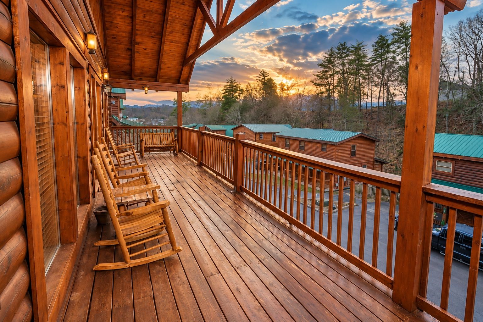 A wooden deck with rocking chairs and a view of cabins in the distance.