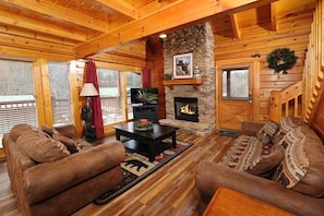 A cozy log cabin interior with a stone fireplace, wooden furniture, and a television.