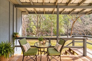 An outdoor patio with two chairs and a table, overlooking a natural landscape with trees and a body of water. - River Reflections: Where Water Mirrors Mountains (Sevierville)