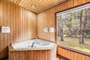 A wooden cabin bathroom with a freestanding bathtub, towels hanging on hooks, and a window overlooking a forested area. - River Reflections: Where Water Mirrors Mountains (Sevierville)