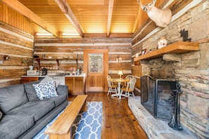 A log cabin interior with a sofa, dining table, chairs, a fireplace, and a kitchen area. - River Reflections: Where Water Mirrors Mountains (Sevierville)