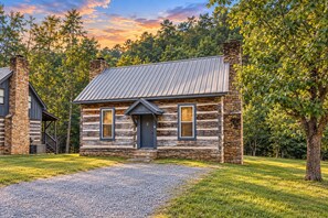 A log cabin with a metal roof, stone chimneys, and a gravel driveway. - River Reflections: Where Water Mirrors Mountains (Sevierville)