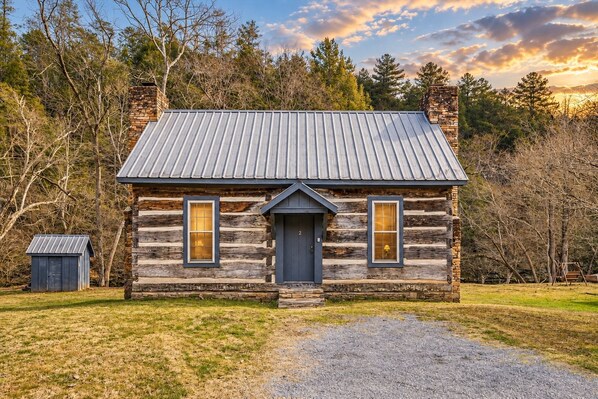 A log cabin with a metal roof, a front door, and two windows. - River Reflections: Where Water Mirrors Mountains (Sevierville)