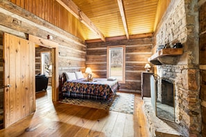 A log cabin room with a bed, a fireplace, and a window. - River Reflections: Where Water Mirrors Mountains (Sevierville)