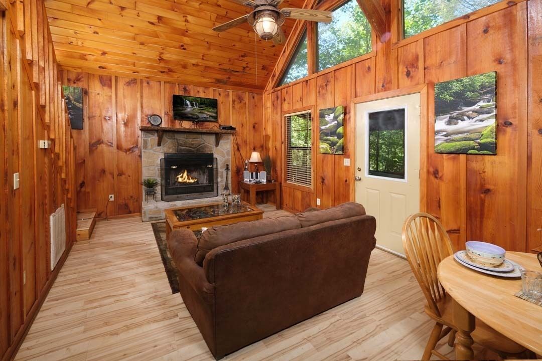 A cozy cabin interior with a fireplace, wooden walls, a sofa, and a dining area.