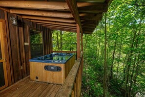 A wooden deck with a hot tub, surrounded by dense forest.