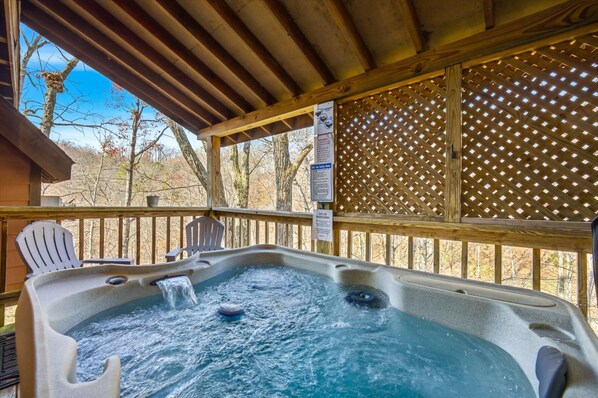 Ein Whirlpool auf einer Holzterrasse mit Stühlen, umgeben von einem Spalierzaun und Bäumen.