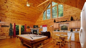 Ein gemütliches Blockhaus-Interieur mit Billardtisch, Kamin, Essbereich und Küche.