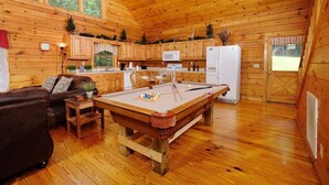 Ein Holzblockhaus-Interieur mit Billardtisch, einer Couch und einer Küchenzeile.