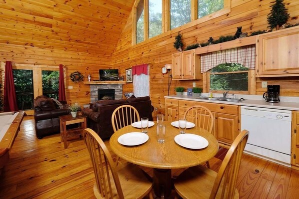 A wooden cabin interior with a dining area, kitchen, and living room.