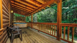 Eine Holzterrasse mit Whirlpool, Holzgeländern und Blick auf einen Wald.