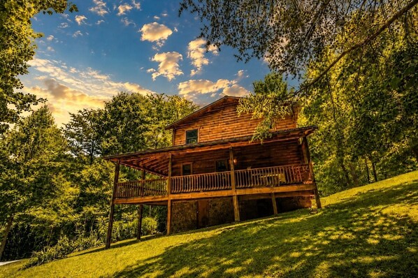 A wooden cabin with a balcony, surrounded by lush greenery and trees. - Above and Beyond: Elevate Your Mountain Escape (Sevierville)