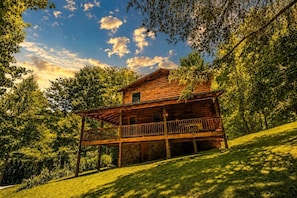 A wooden cabin with a balcony, surrounded by lush greenery and trees.