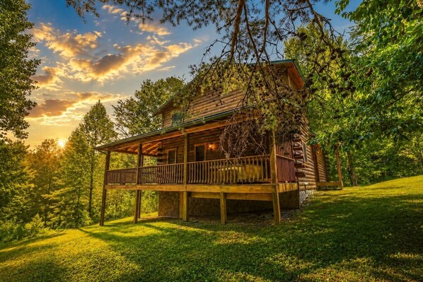 A wooden cabin with a balcony, surrounded by trees and a grassy area.