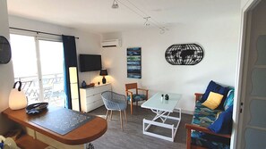 A modern living room with a sofa, chairs, a small table, a TV, and a balcony with a railing.