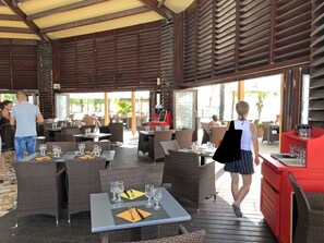 Restaurante ao ar livre com móveis de vime e mesas preparadas para refeições.