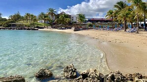 A beach with clear water, palm trees, and a building with a red roof.