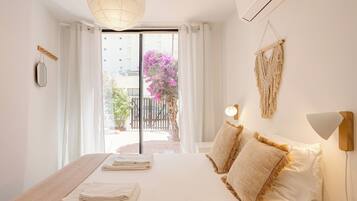 A bedroom with a bed, a bedside lamp, and a view of a balcony with a potted plant.