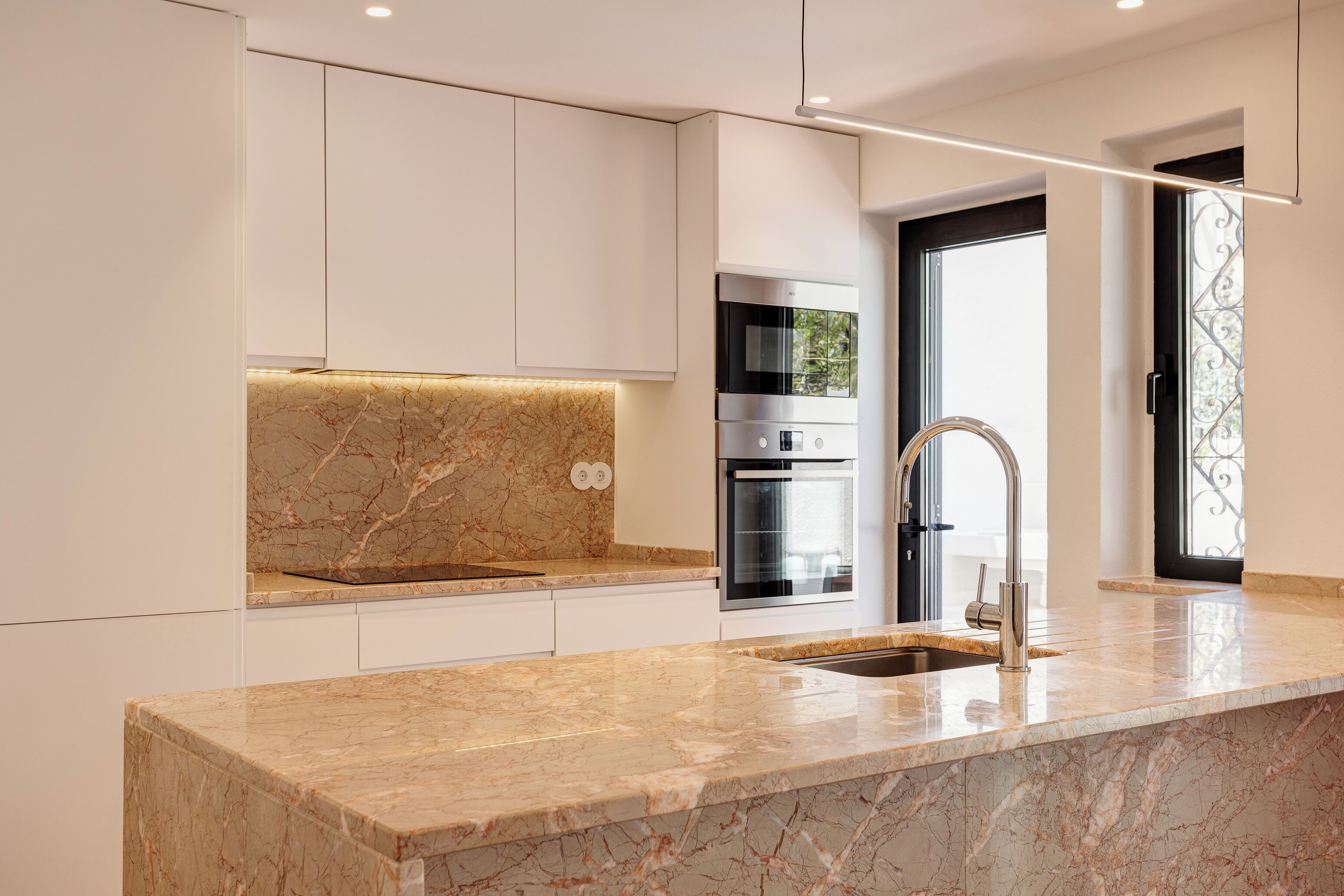 A modern kitchen with white cabinetry, a marble countertop, and stainless steel appliances.